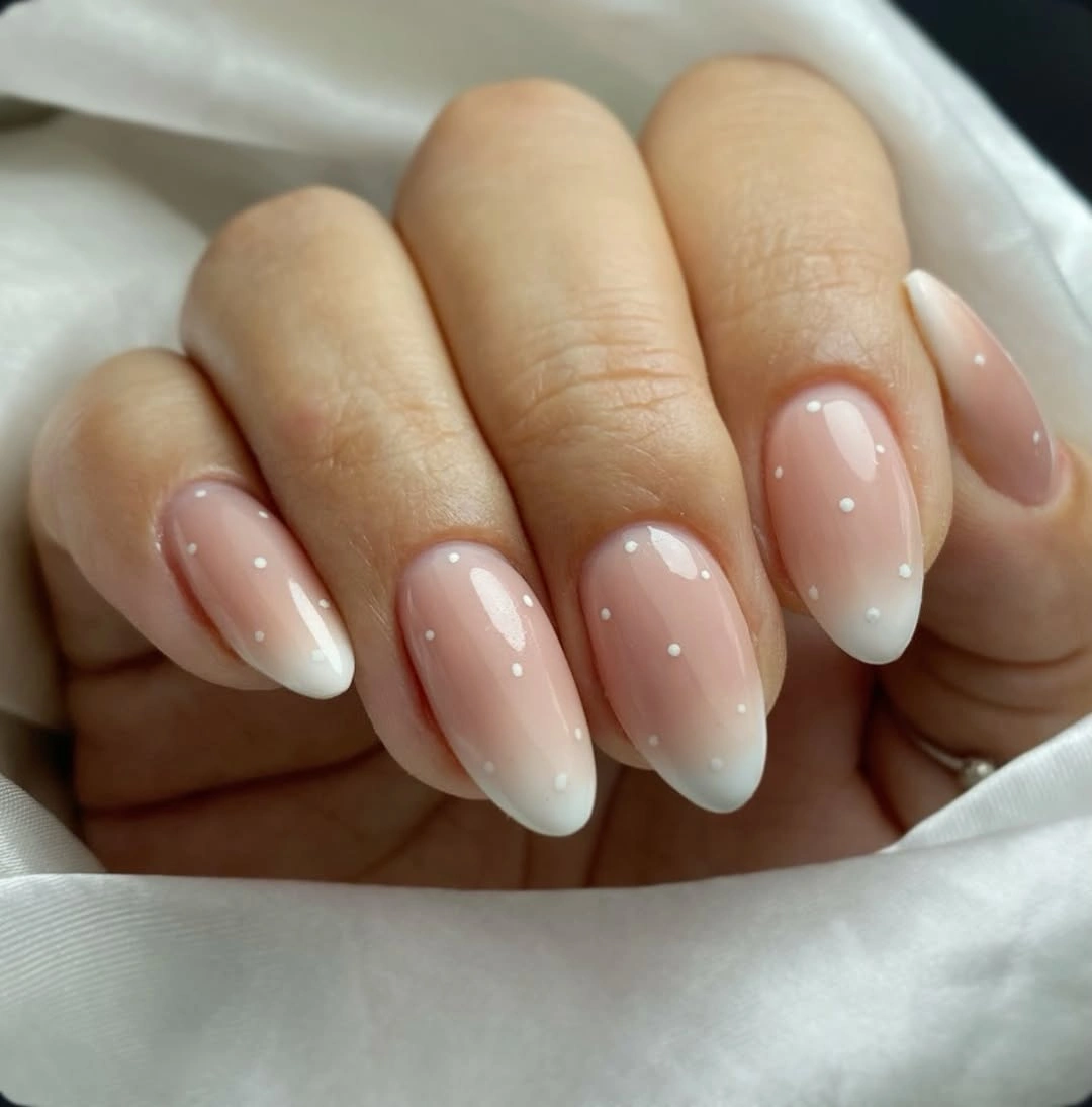 Soft nude almond nails with tiny pale dotted accents near light tips