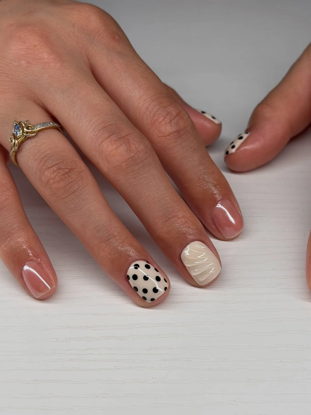 short peach nails with one black and white polka dot accent