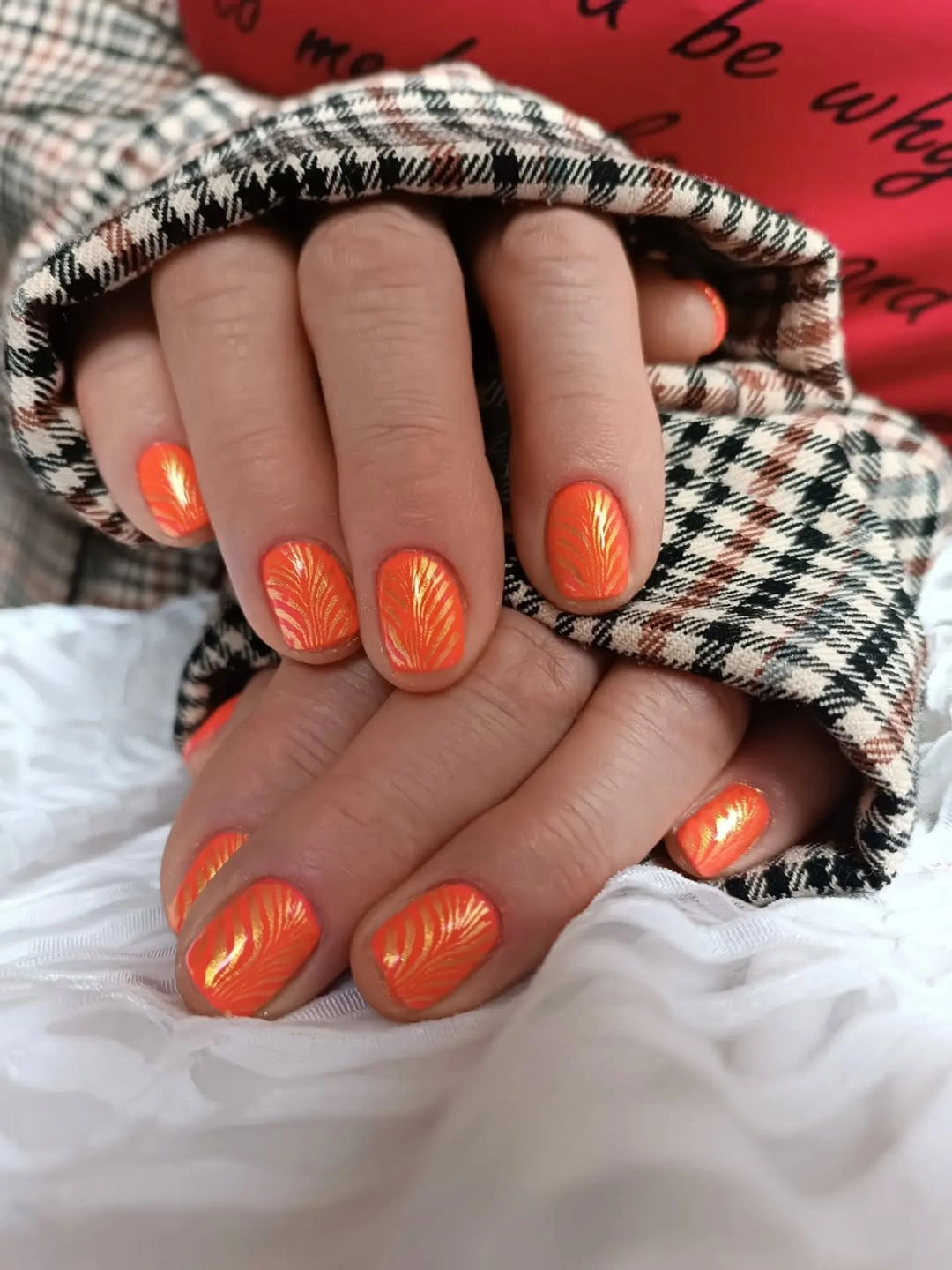 short glossy orange nails with lighter curved line accents