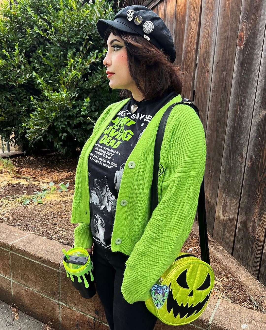 Neon green cardigan over black graphic shirt and black trousers with green pumpkin bag and animal-ear beret