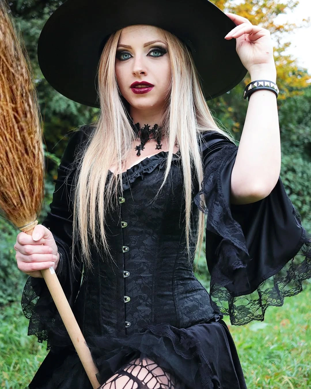 Black corset witch outfit with lace sleeves fishnet tights wide-brim hat and broom