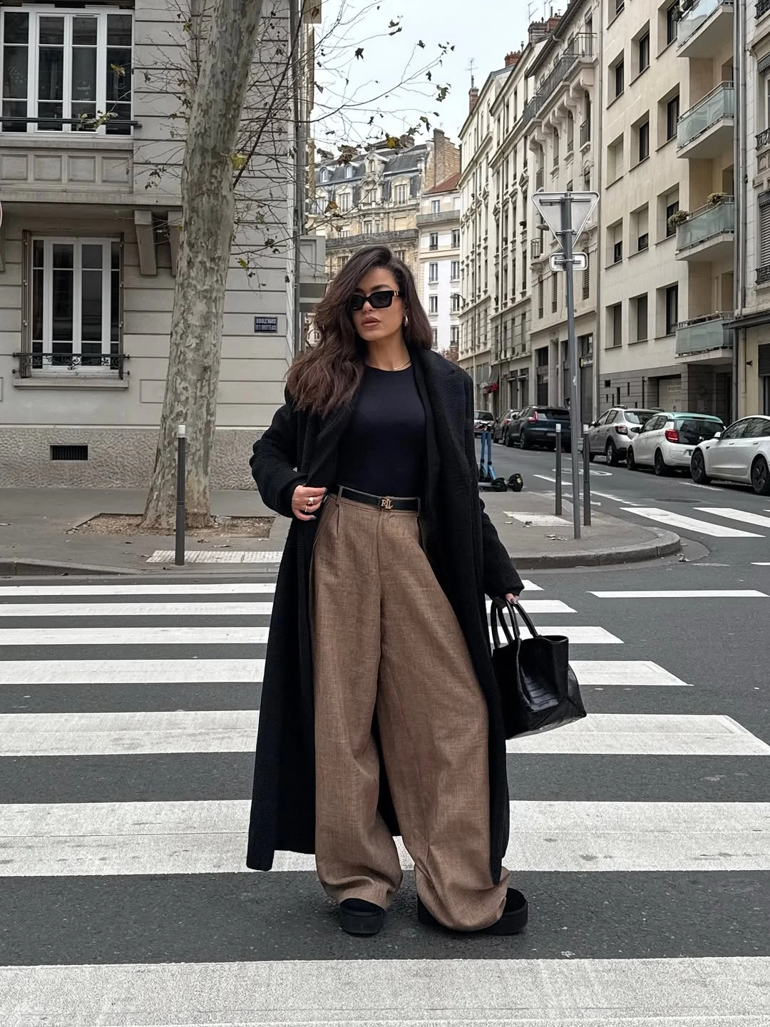 Long black coat black fitted top taupe wide trousers and black handbag