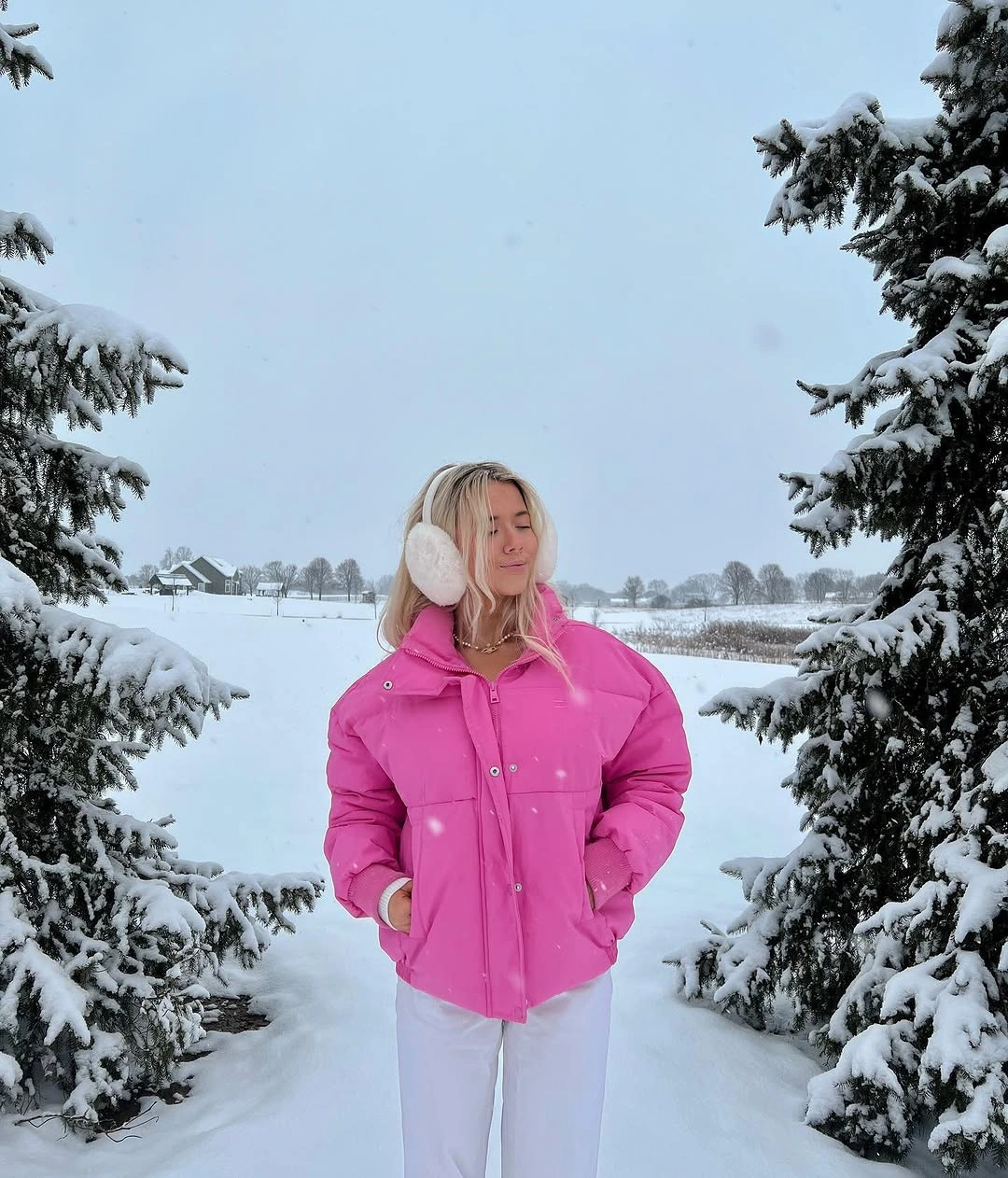 Woman in bright pink puffer jacket white pants and earmuffs
