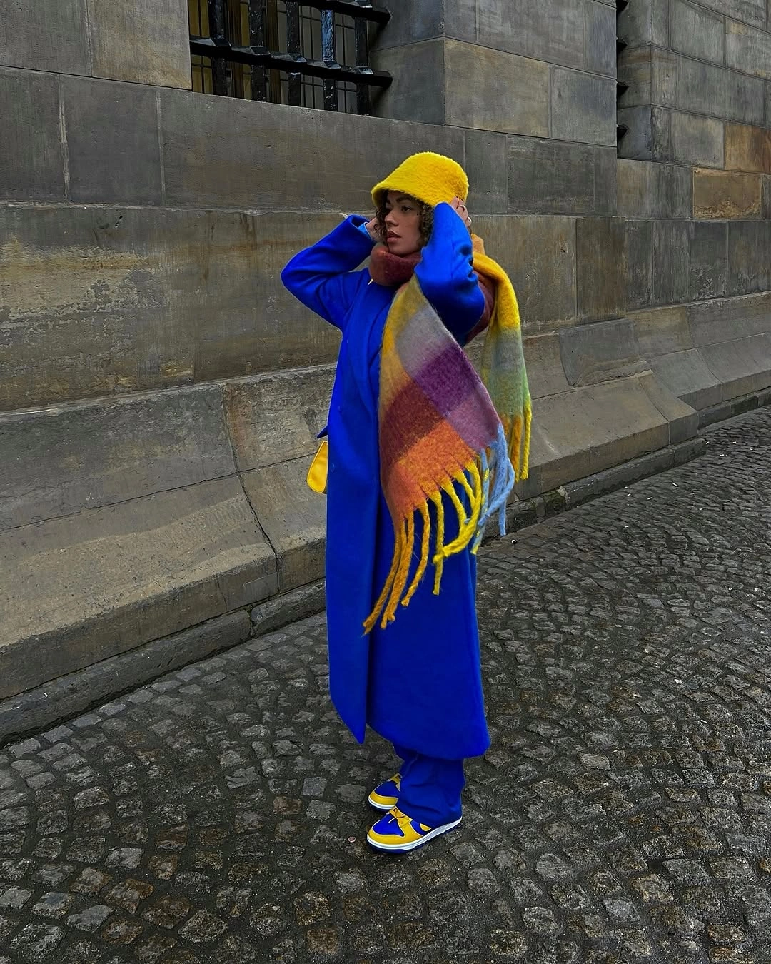 Woman in cobalt coat yellow hat scarf and matching sneakers