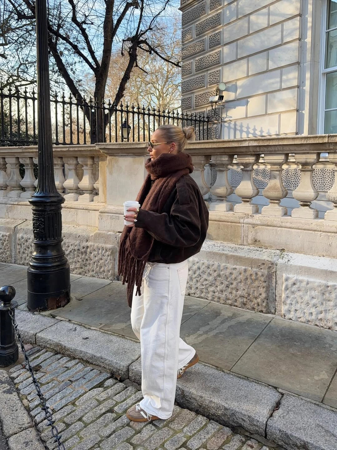 Woman in brown scarf dark sweater white trousers and sneakers