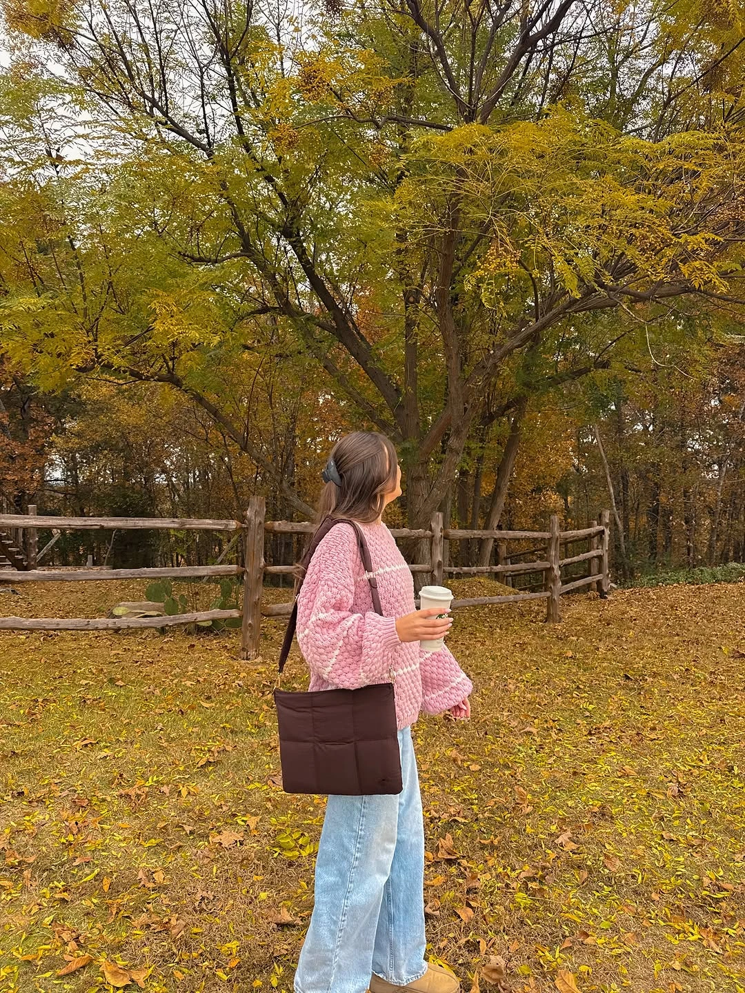 Woman in pink quilted jacket light jeans and brown tote outdoors