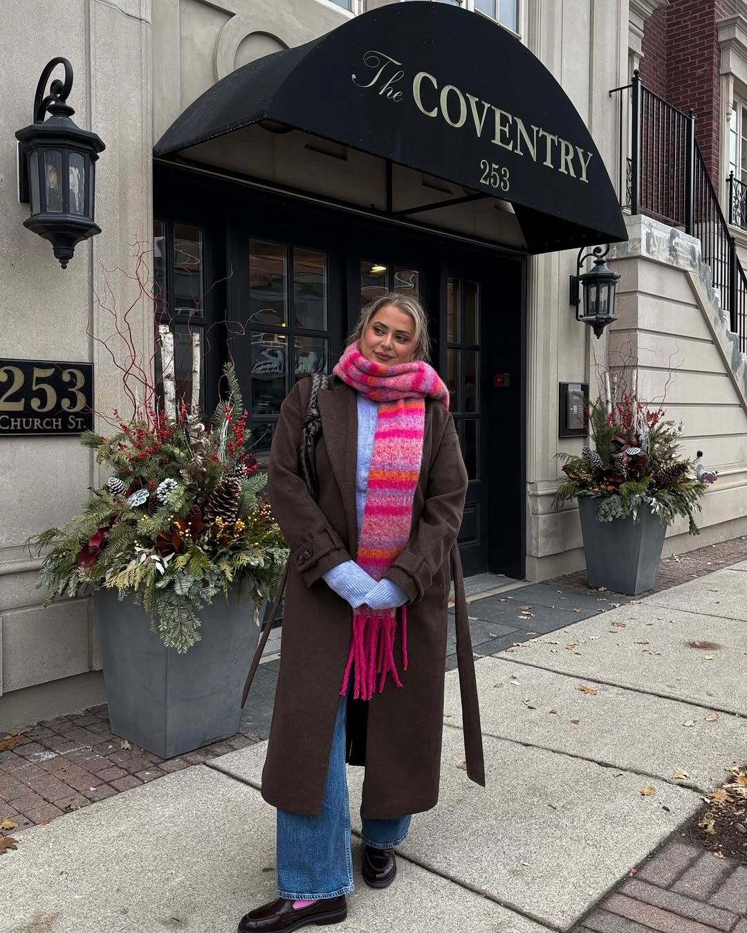 Woman in long brown coat bright striped scarf and blue jeans