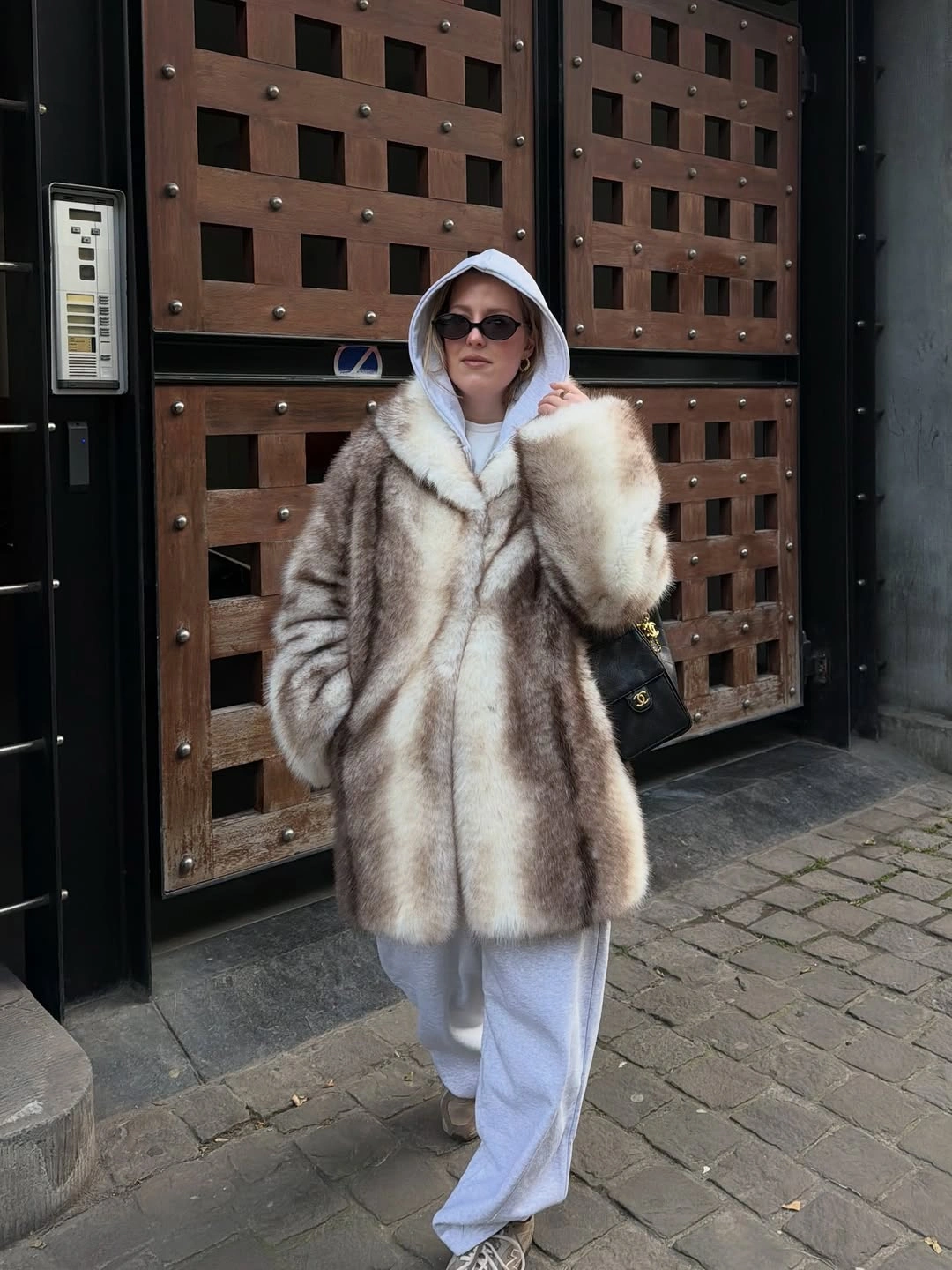 Woman in soft hooded coat pale joggers and sunglasses outdoors