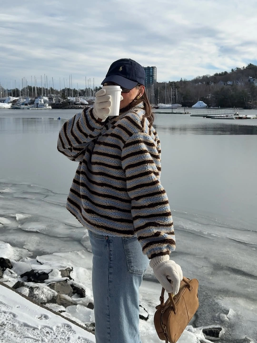Woman in striped sweater jeans gloves and cap by icy water
