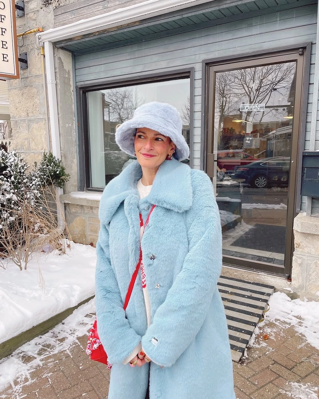 Woman in powder blue coat fluffy hat and red crossbody bag