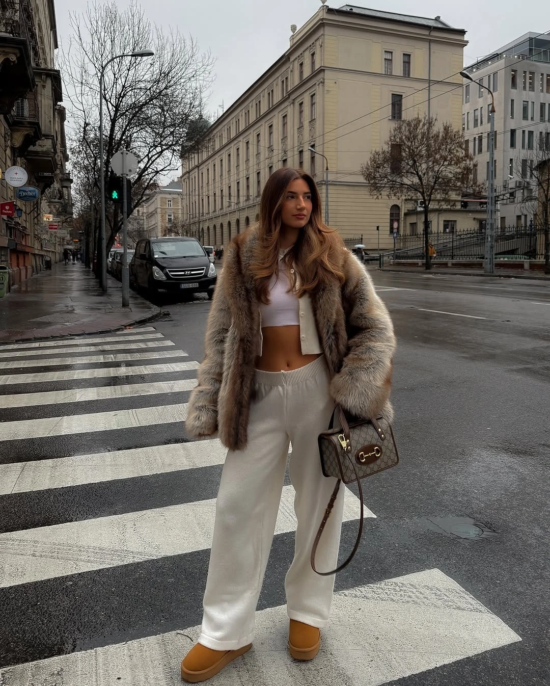 Woman in brown faux fur jacket white crop top and trousers