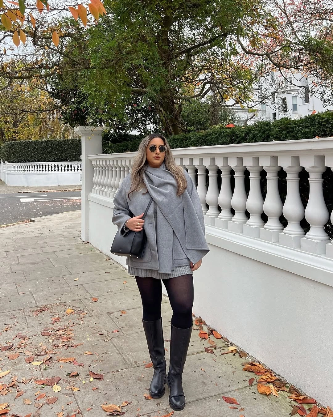 Gray jacket and short skirt with sheer tights, knee-high boots, and black bag