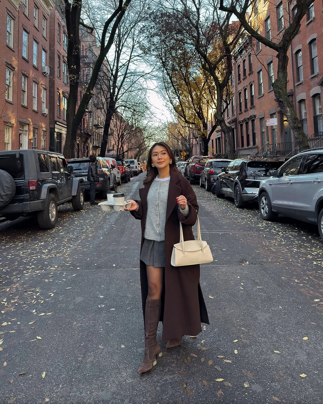 Long brown coat with gray skirt, knee-high boots, and pale handbag