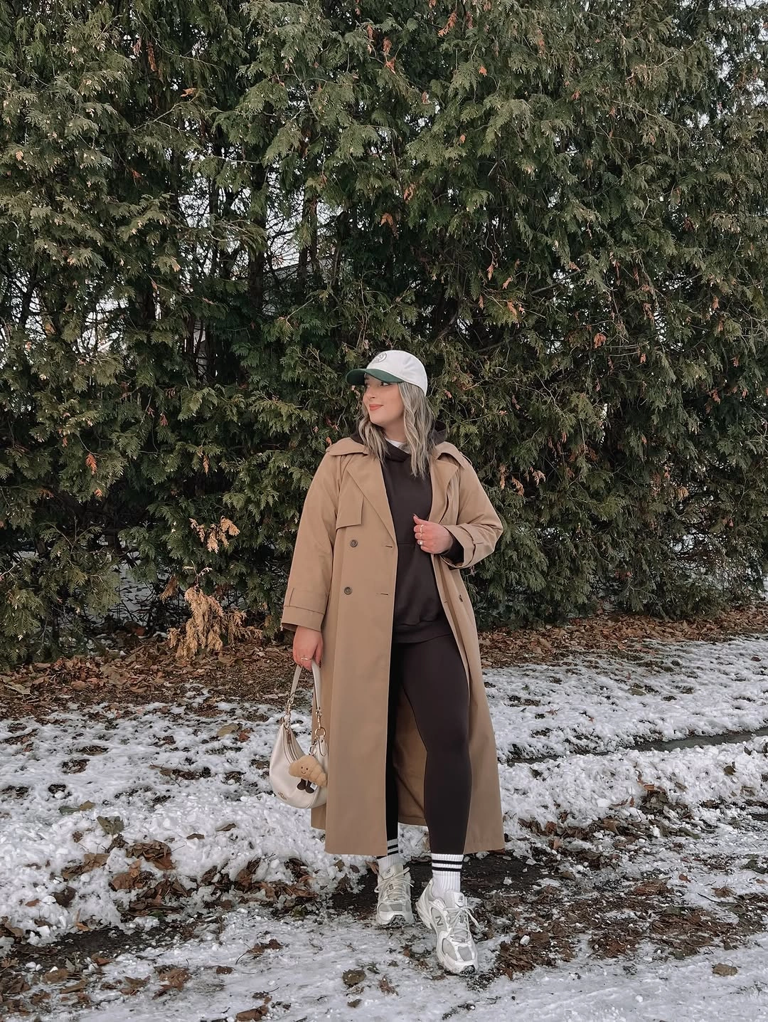 Camel coat with brown top, loose trousers, cap, sneakers, and pale bag