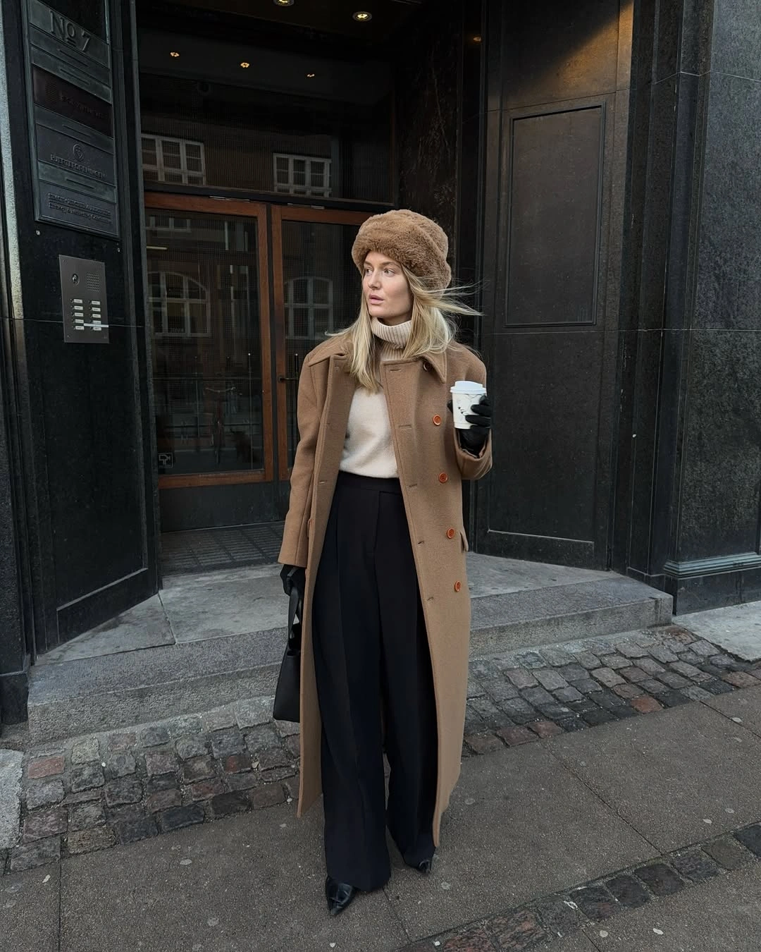 Long brown coat with light high-neck top and wide black trousers