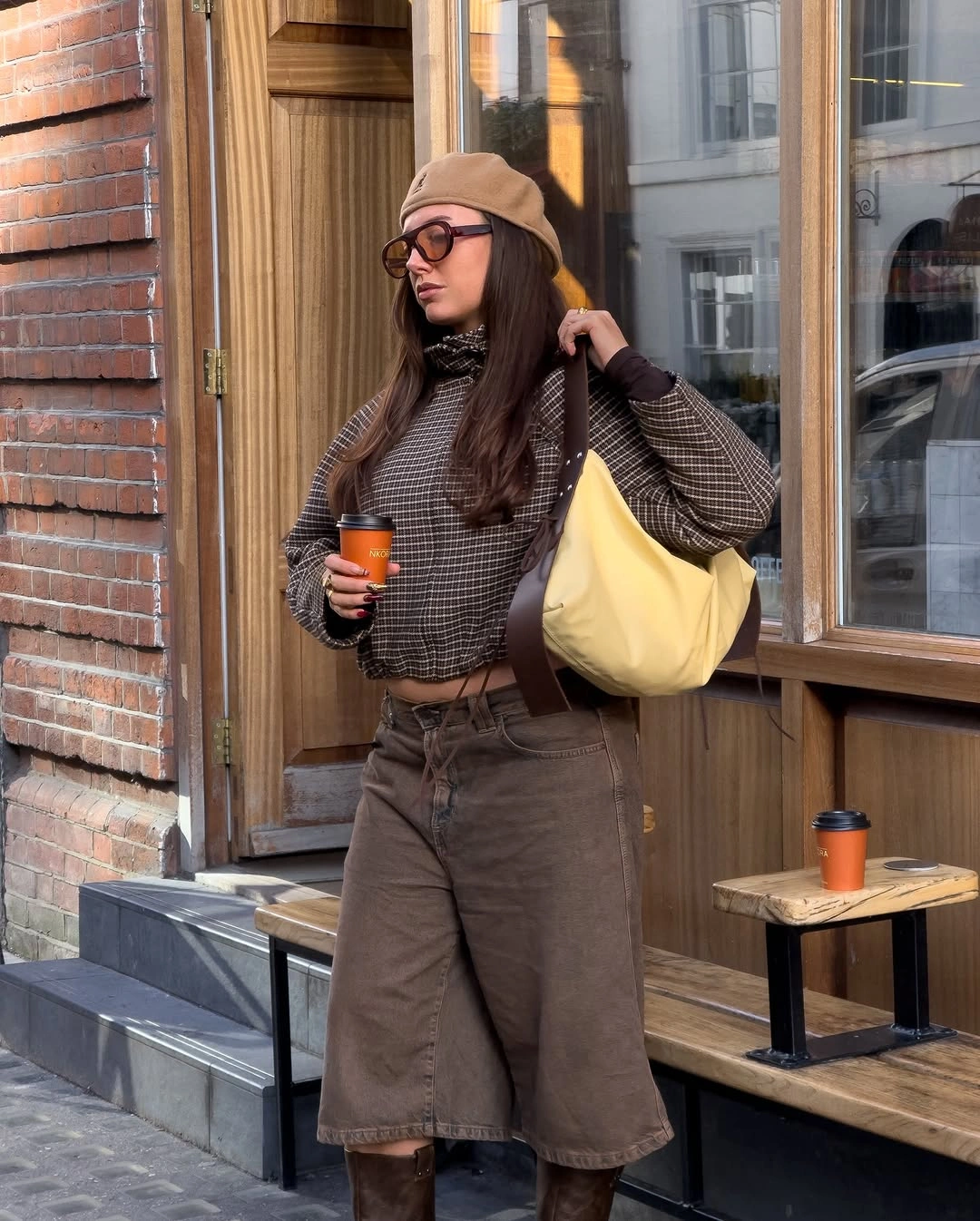 Brown patterned top with long shorts, tall boots, beanie, and yellow bag