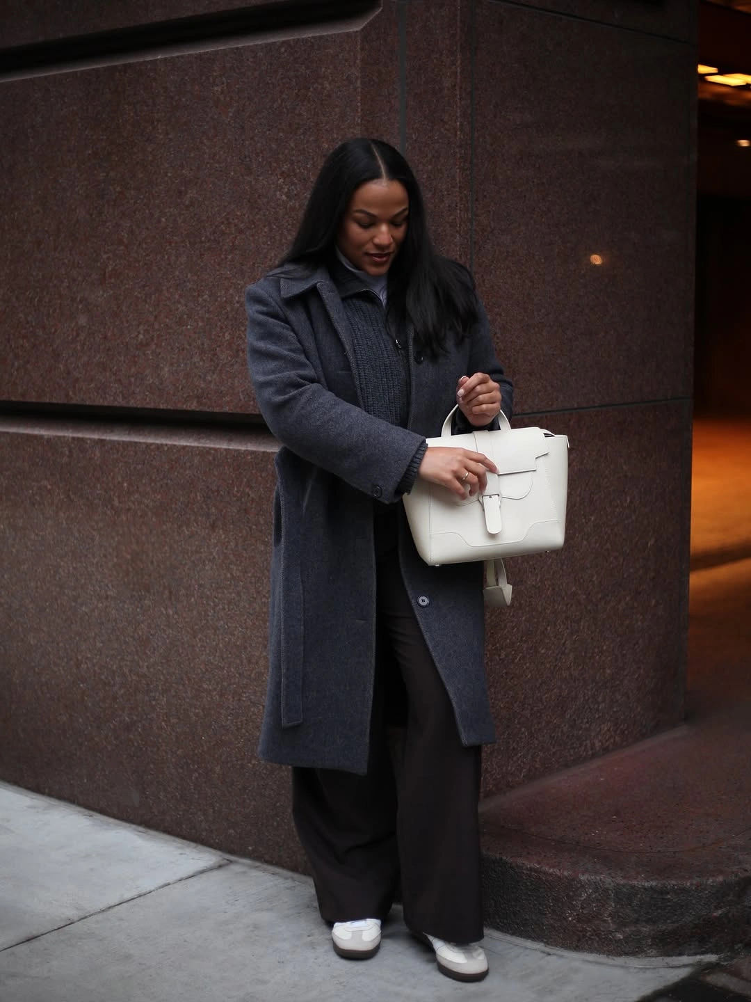 Charcoal long coat with wide black trousers, white bag, and sneakers