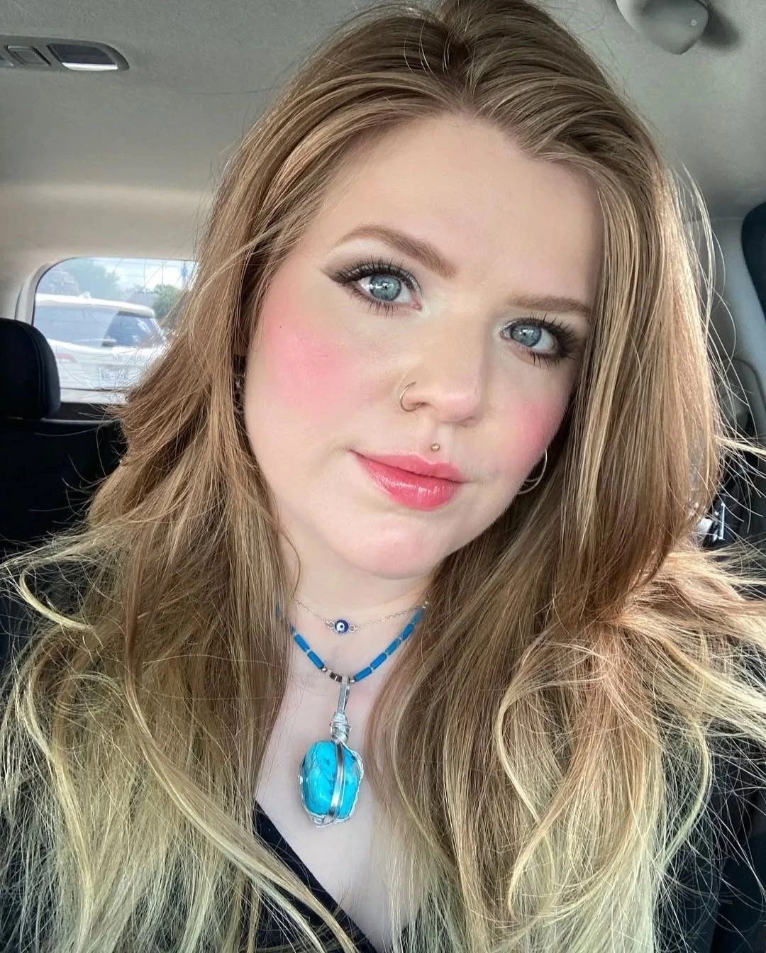 Long blonde layered hair with turquoise pendant in car