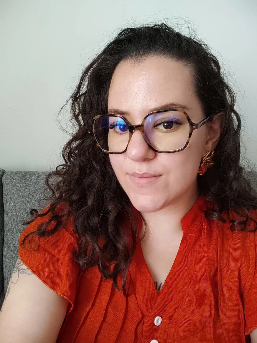 Shoulder-length dark curls with glasses and red-orange blouse