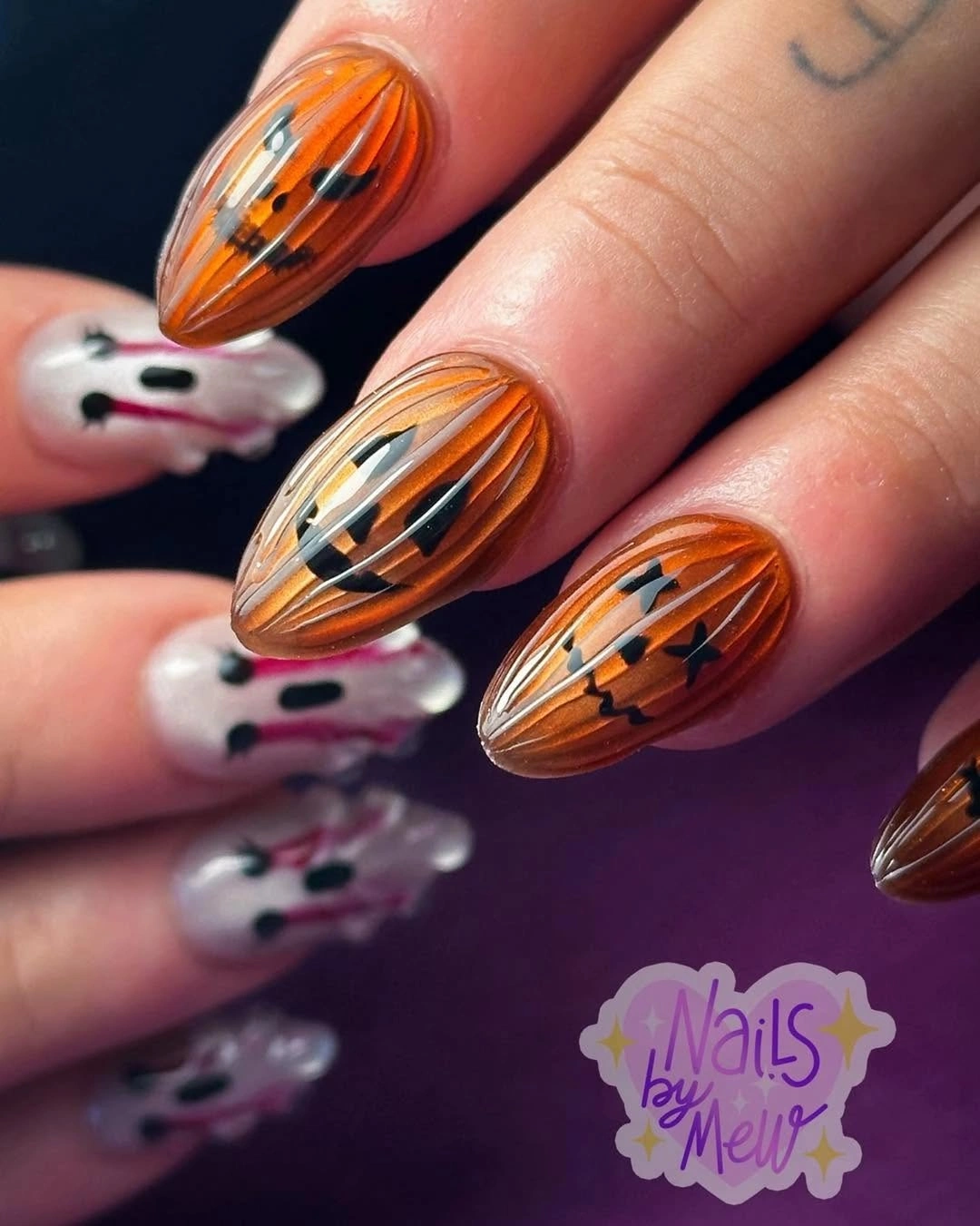 Glossy orange almond nails painted as pumpkins with black lines