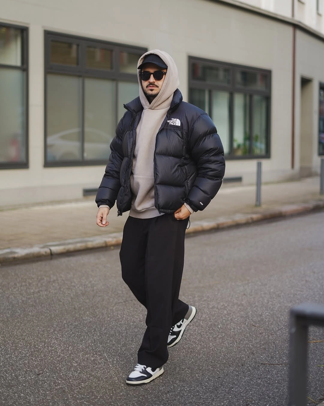 Black puffer over gray hoodie black trousers cap and sneakers