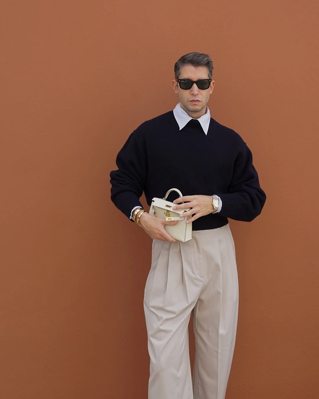 Navy sweater over white collar with cream pleated trousers and loafers