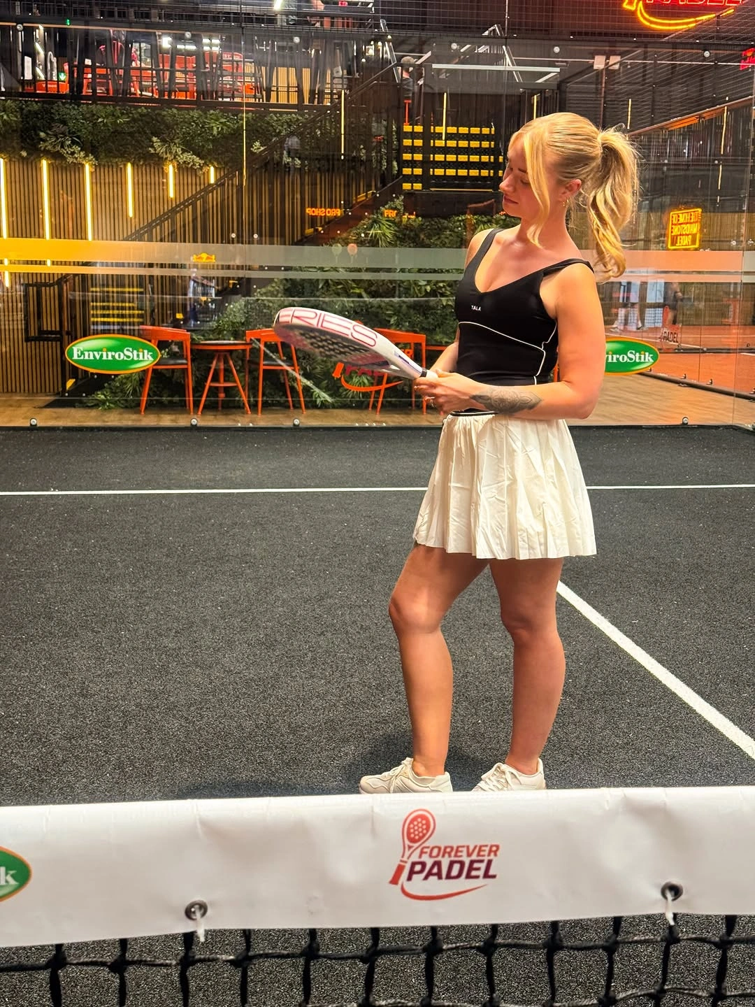 Black fitted tank cream pleated skirt white shoes and padel racket