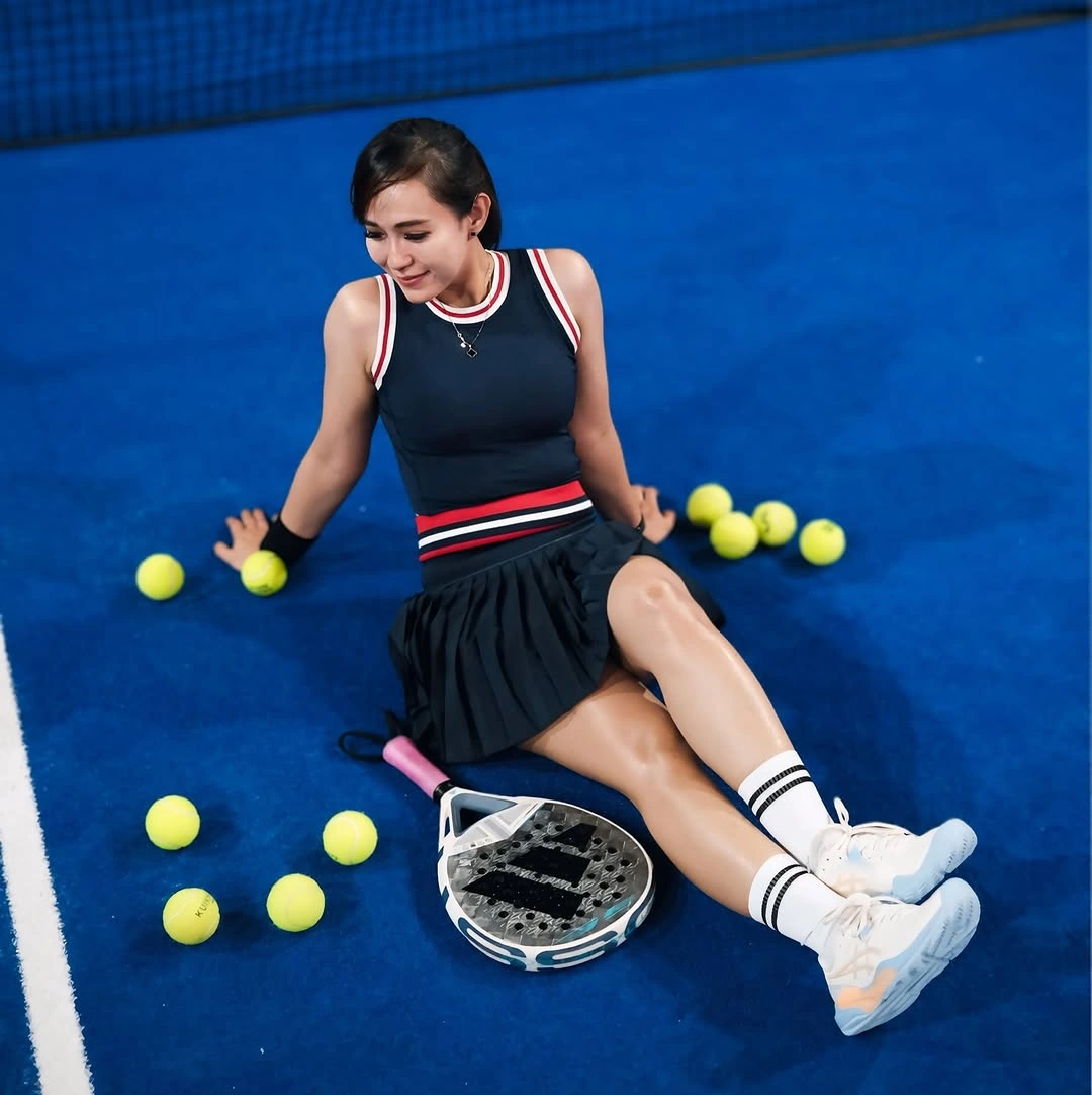 Black athletic tank pleated black skirt striped waistband white shoes and padel racket