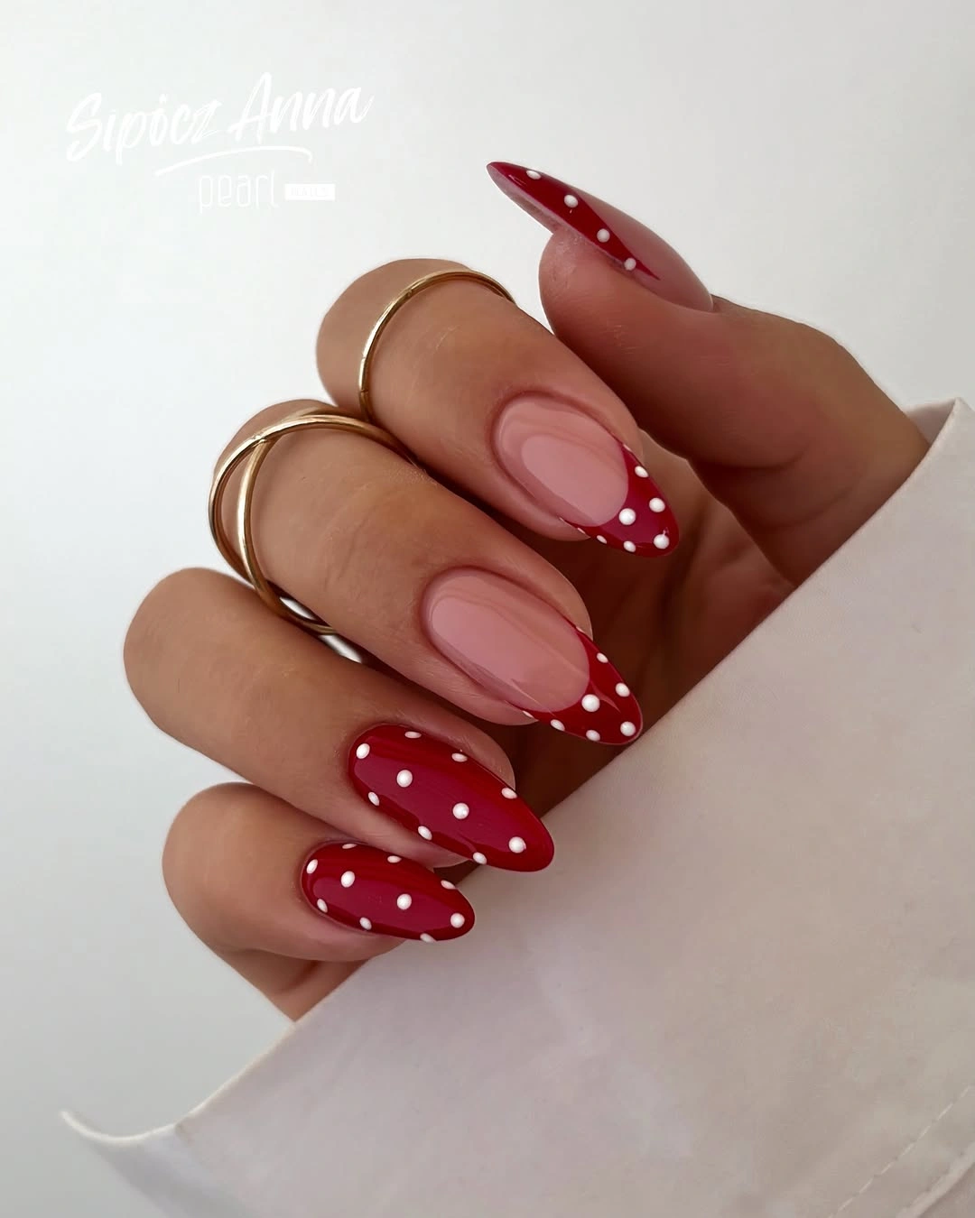Nude almond nails with deep red French tips and white dots