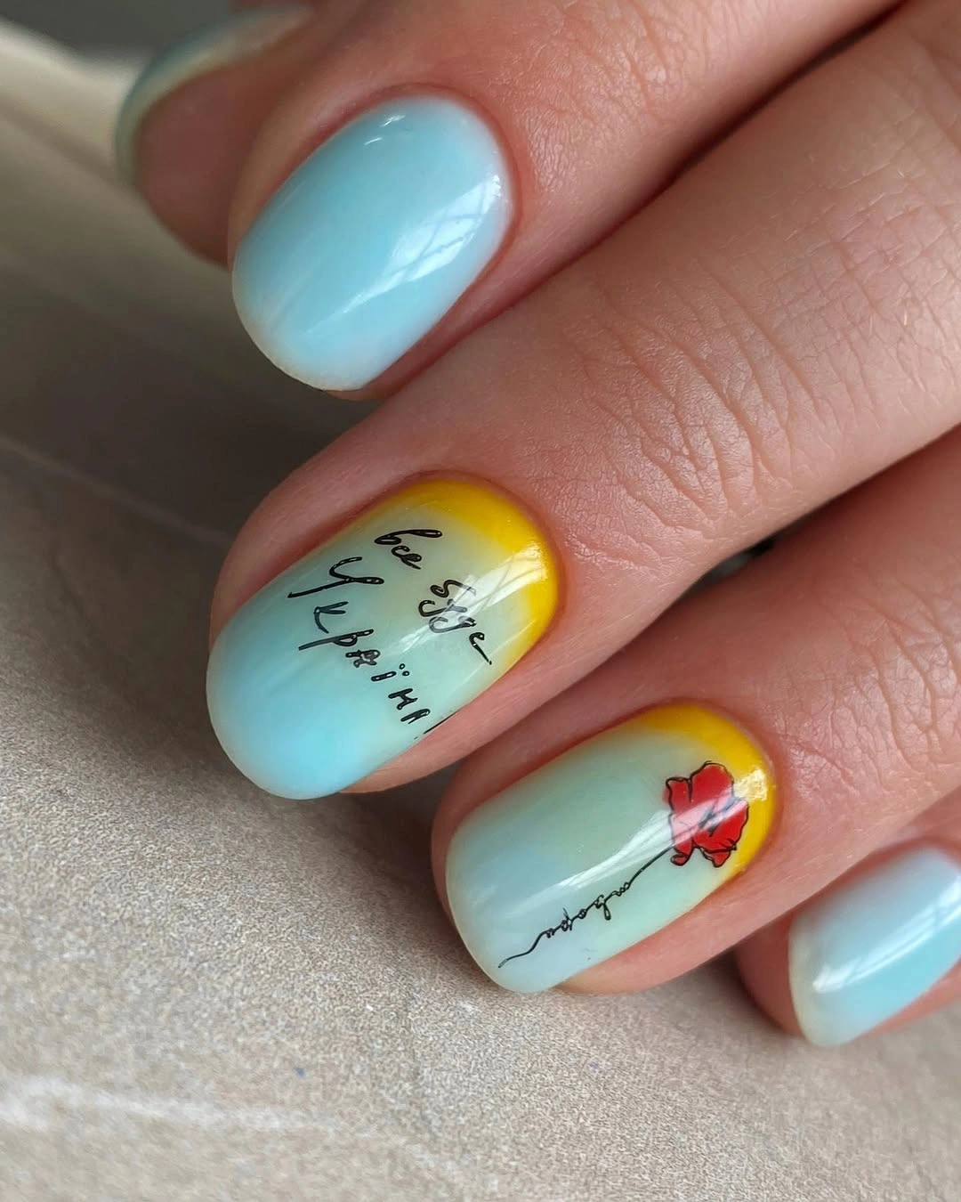 Rounded aqua and yellow nails with script-like marks and red flower