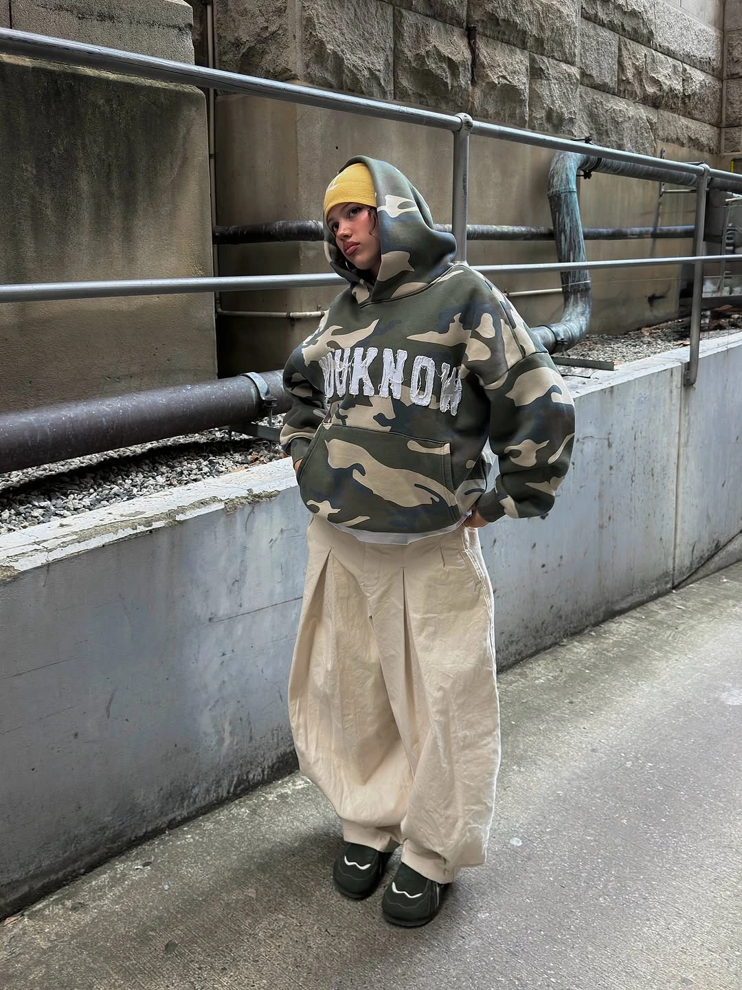 Camo hoodie with cream baggy pants, yellow cap, and dark shoes
