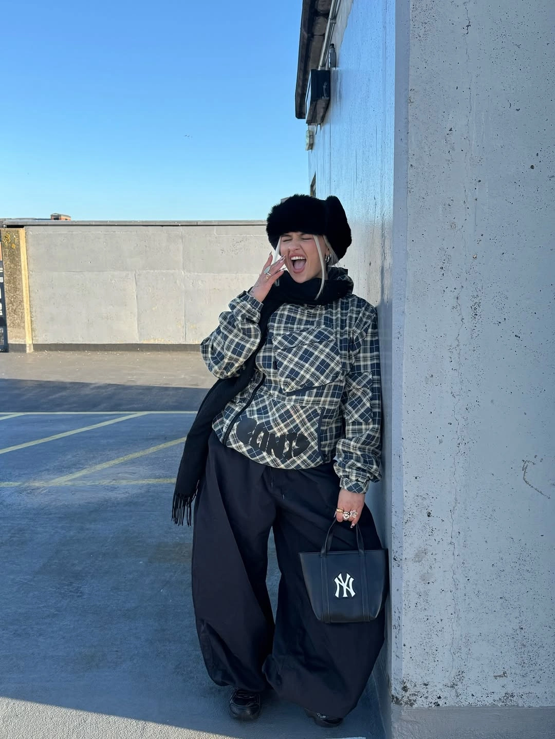 Gray plaid overshirt with wide black trousers, dark scarf, and furry hat