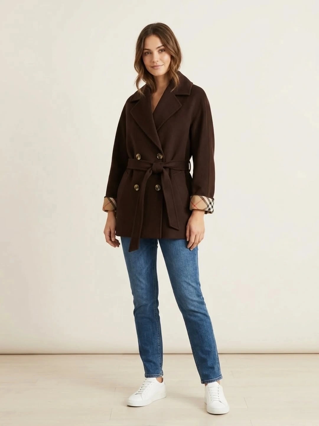 Brown belted double-breasted coat with blue jeans and white sneakers