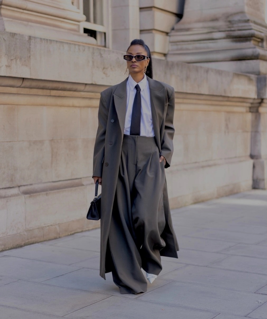 Gray tailored coat with white shirt black tie and wide trousers
