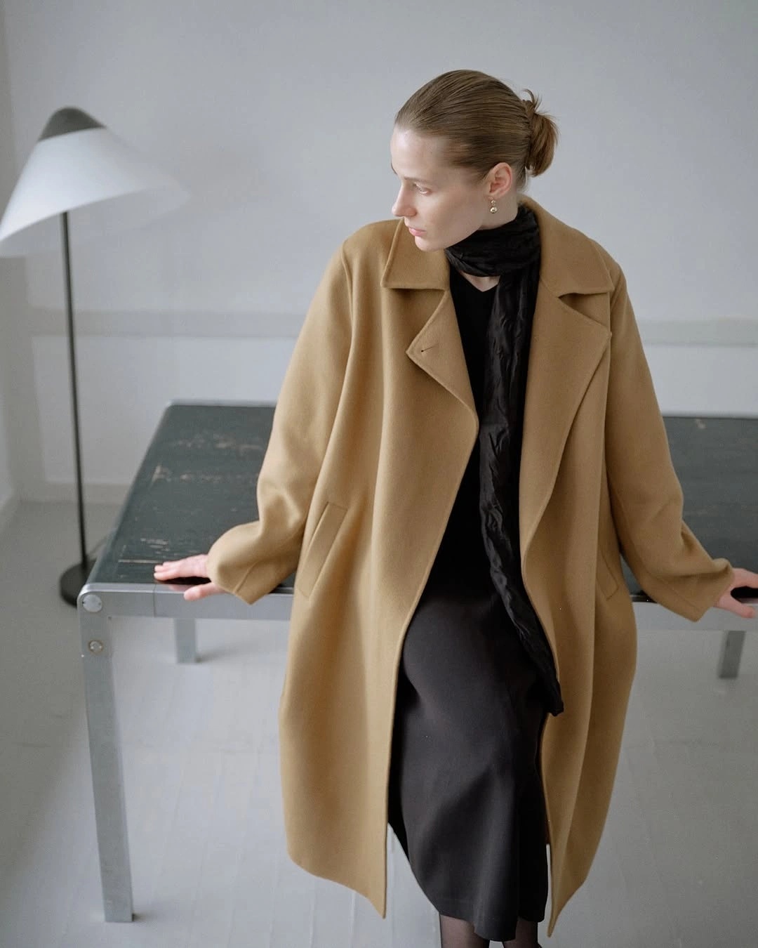 Camel long coat with black scarf and dark trousers indoors