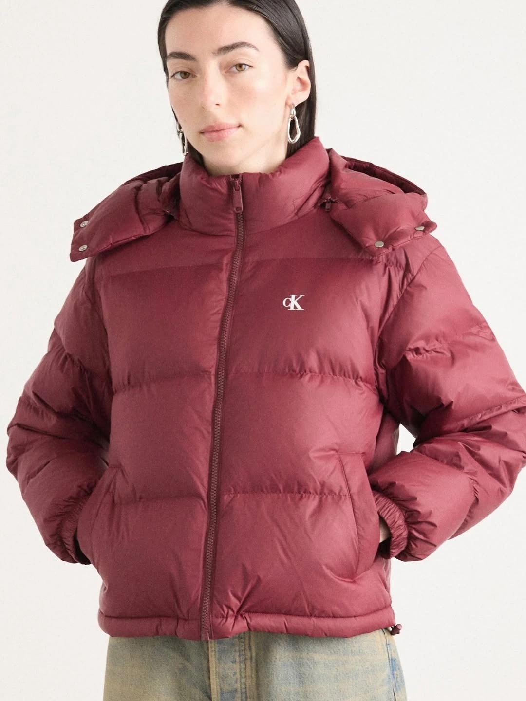 Burgundy hooded puffer jacket with light jeans in studio