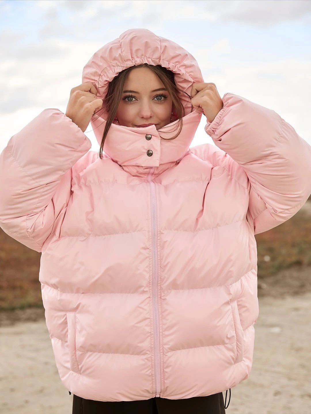 Soft pink hooded puffer jacket with black pants outdoors