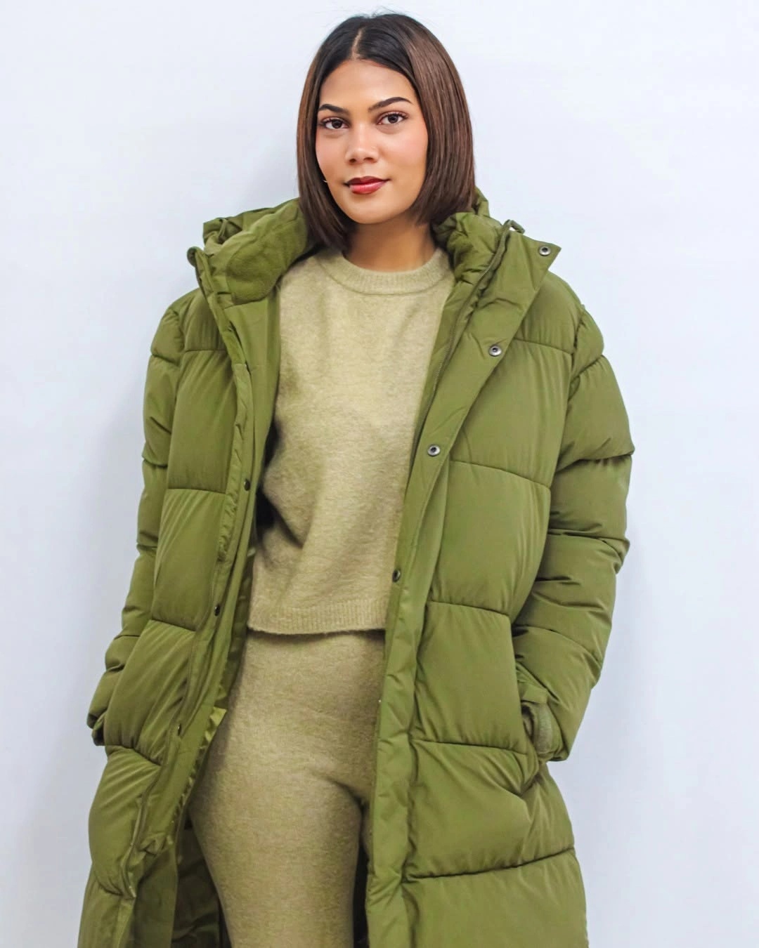 Olive green long puffer jacket over beige knit top and trousers