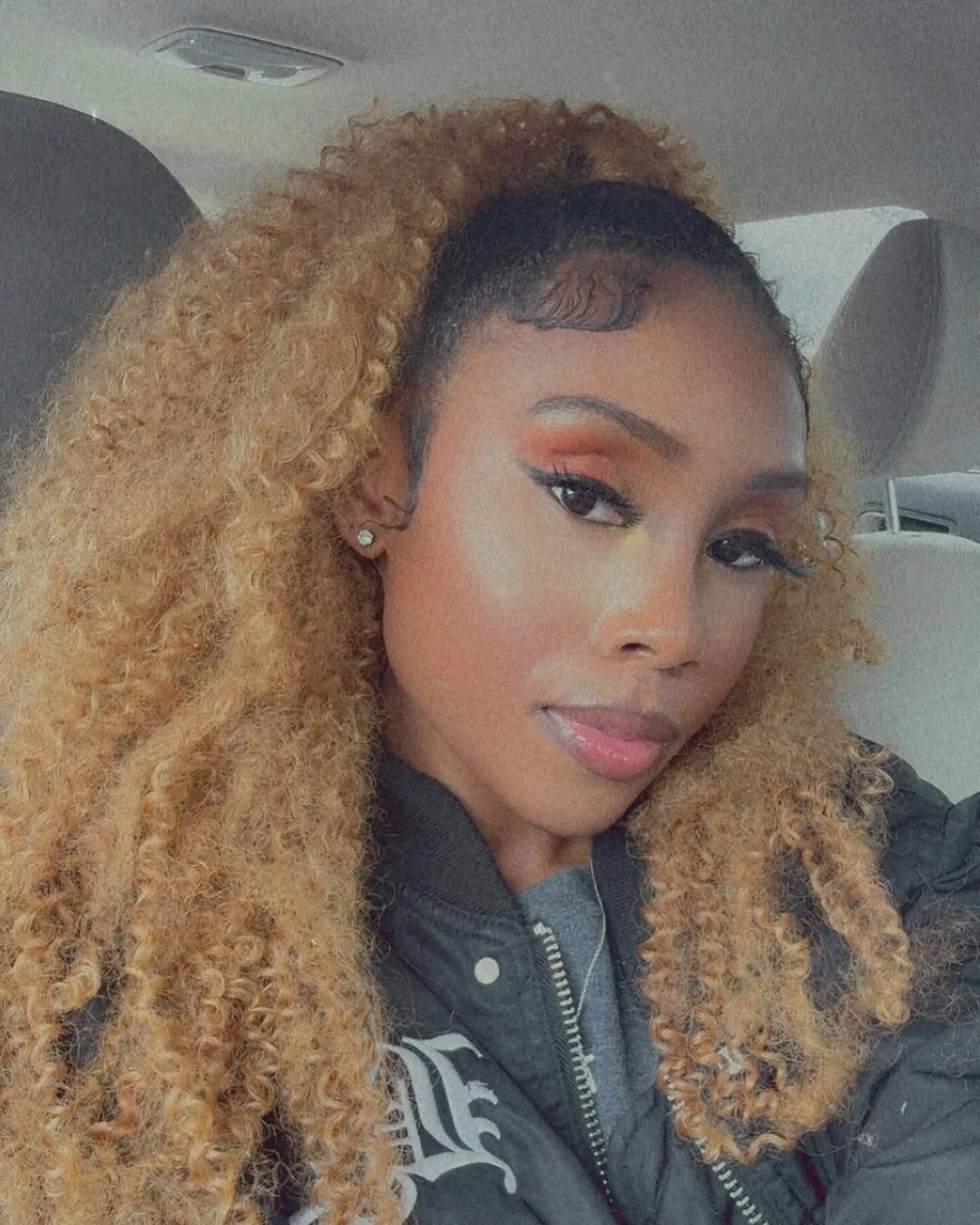 Blonde curly lengths lifted above a sleek dark top
