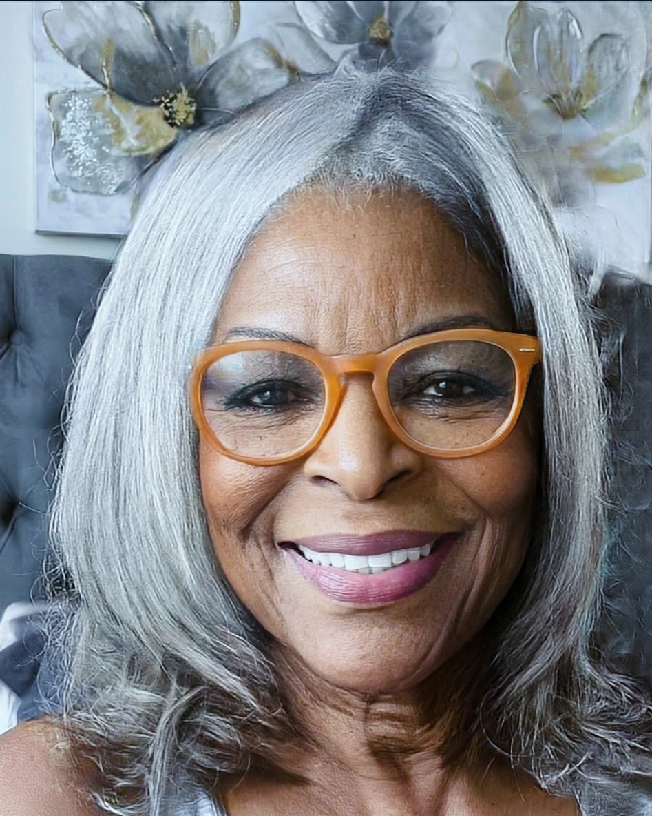 Shoulder-length silver hair with center part and amber glasses