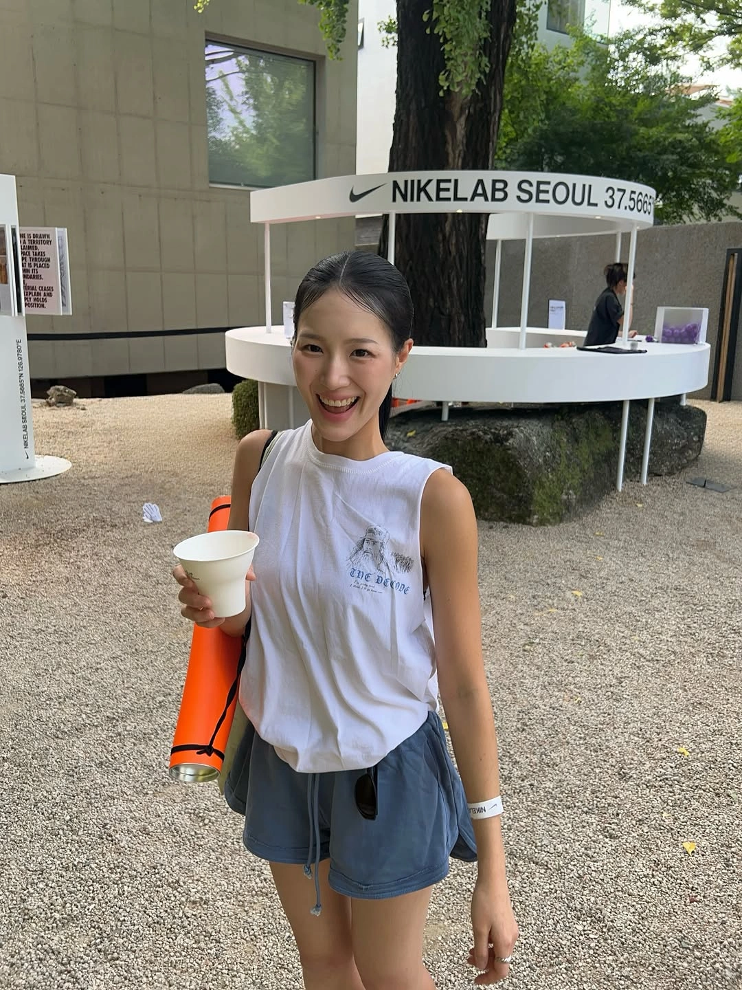 White sleeveless top with blue shorts and orange carry item