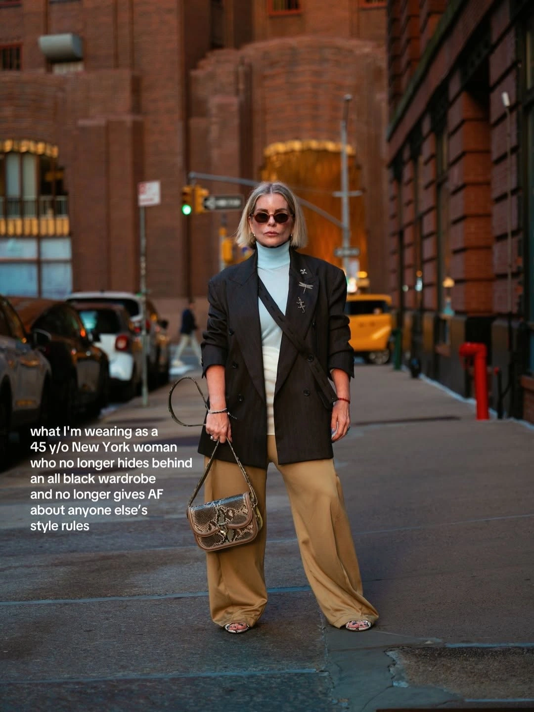 Woman in black blazer with tan wide trousers and patterned handbag