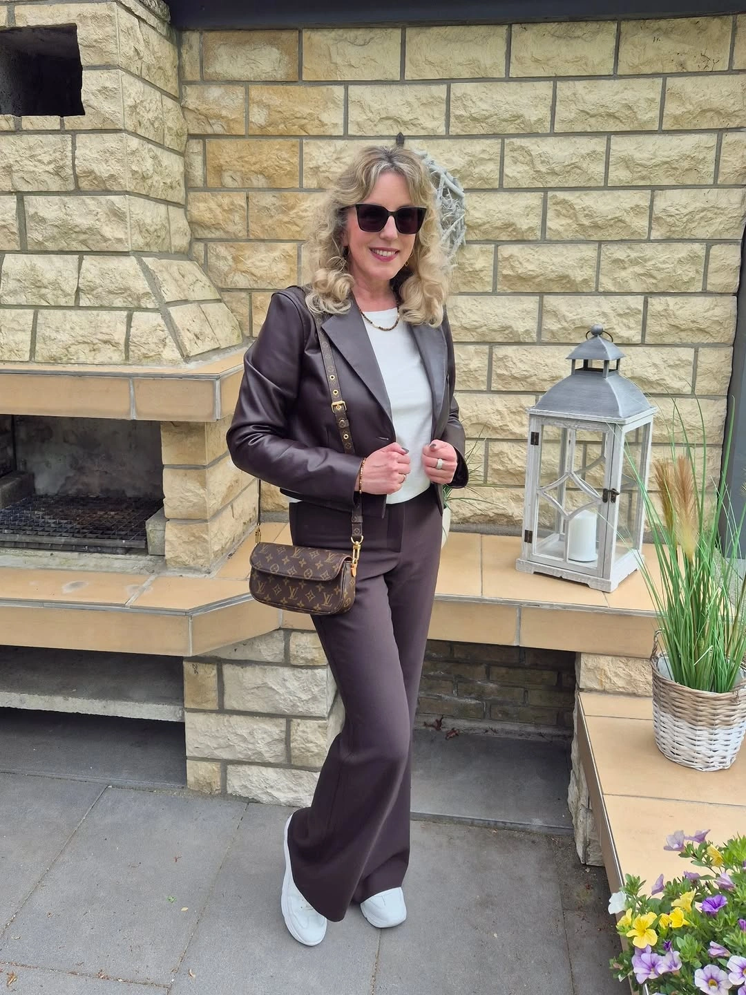 Woman in dark brown jacket trousers and white sneakers