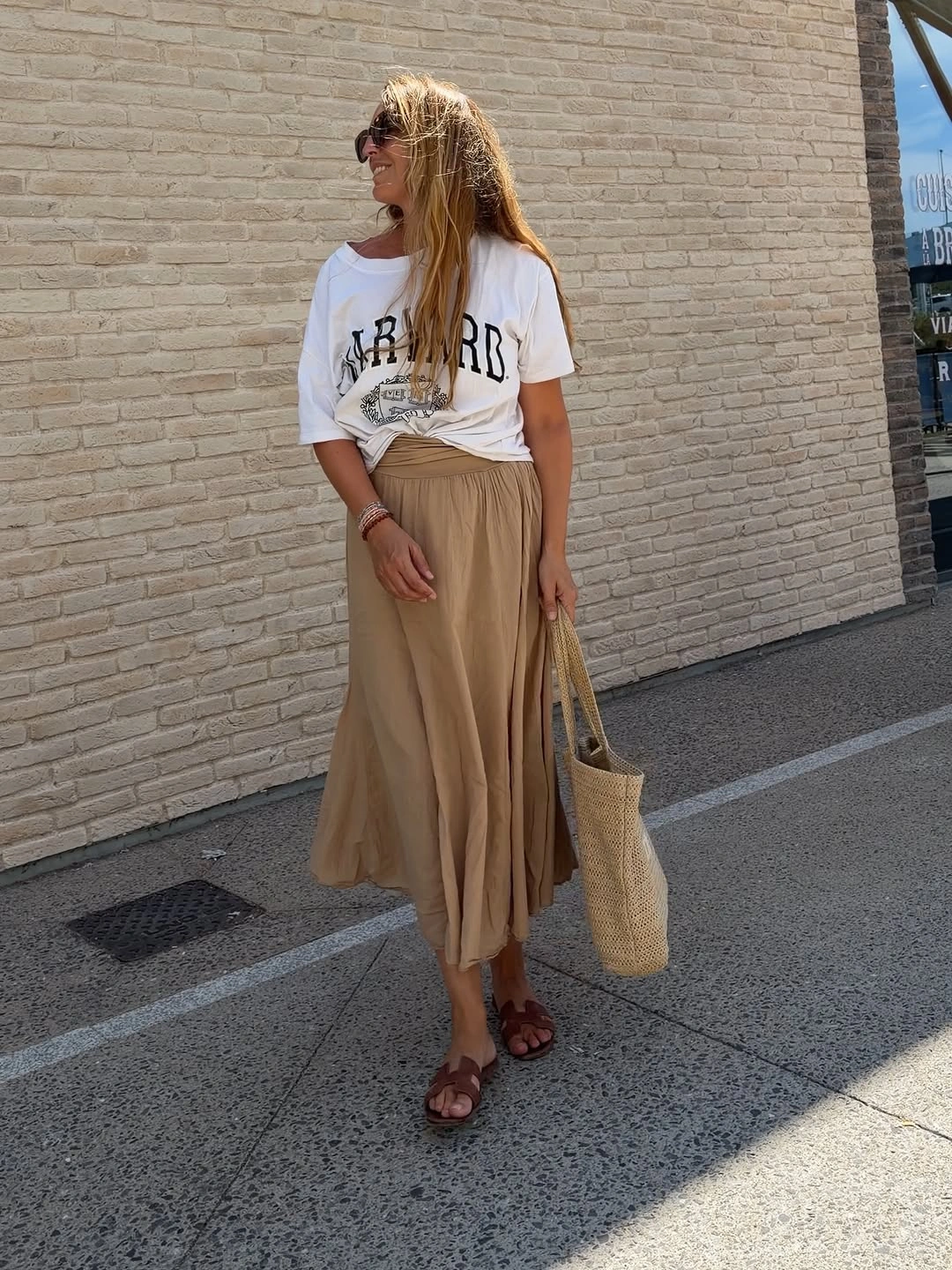 Woman in white graphic tee beige skirt and woven tote