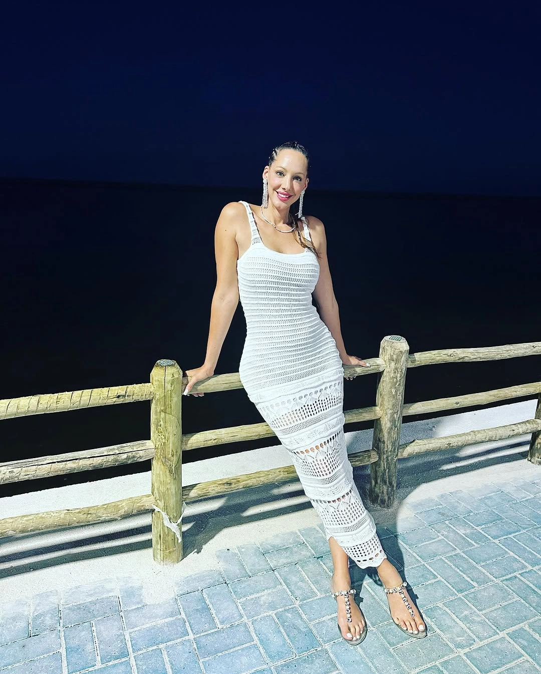 Woman in white openwork dress and strappy sandals by railing