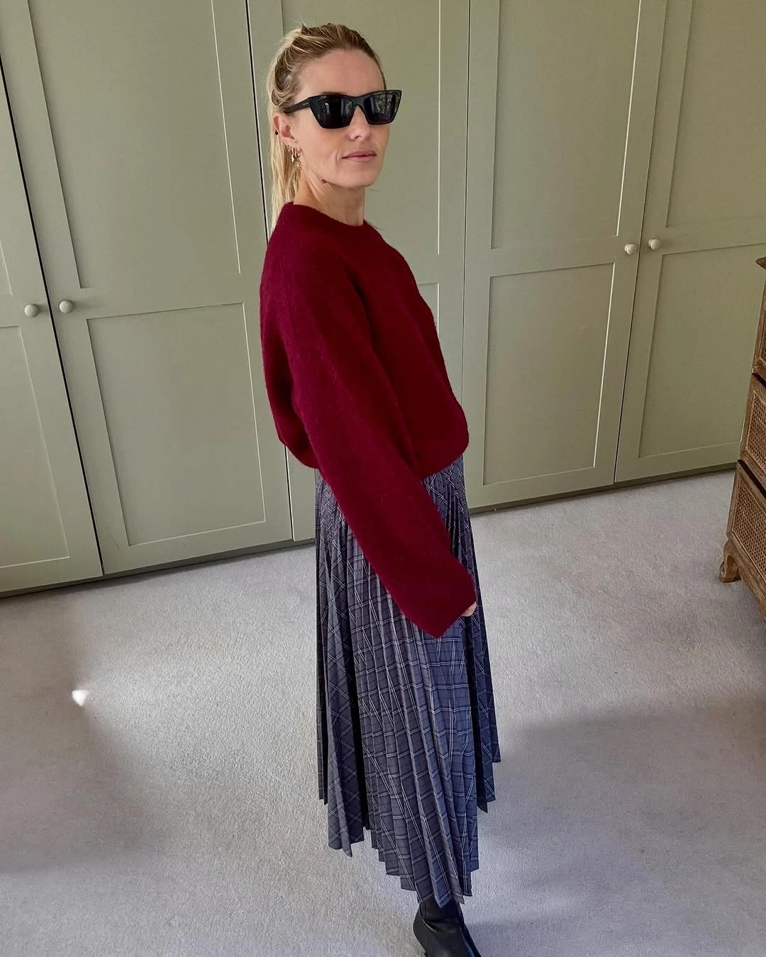 Woman in burgundy sweater gray checked pleated skirt and boots