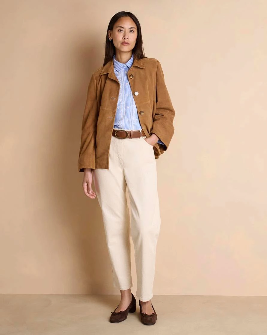 Woman in tan jacket blue shirt cream pants and brown flats