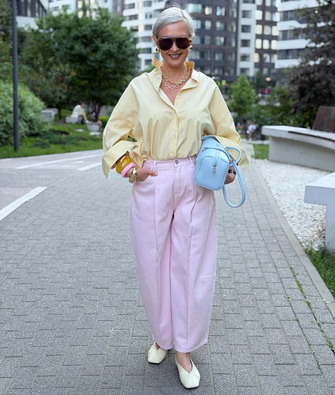 Woman wearing pale yellow shirt pink trousers and blue handbag