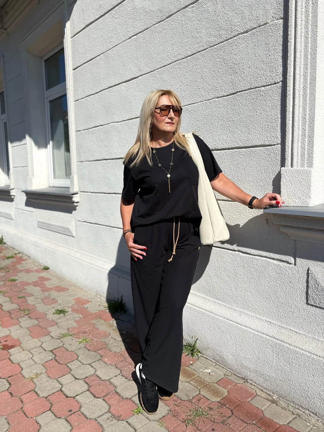 Woman in black top wide black pants sneakers and cream tote