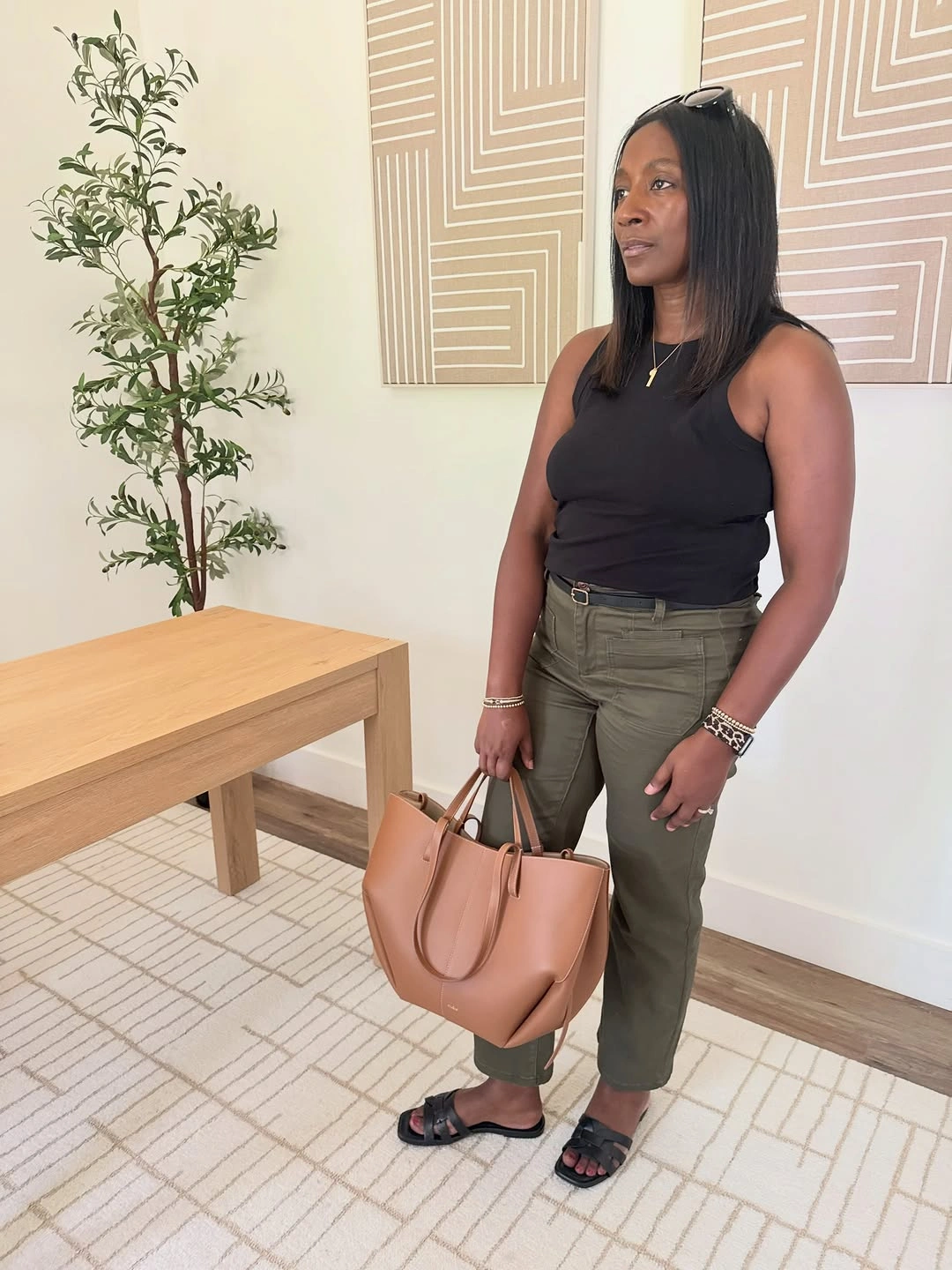 Woman wearing black sleeveless top olive cropped pants and tan tote